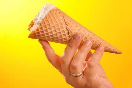 ice cream cone in hand on yellow backgroundの写真素材