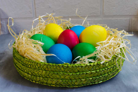 Colored eggs in a green basket on the tableの写真素材