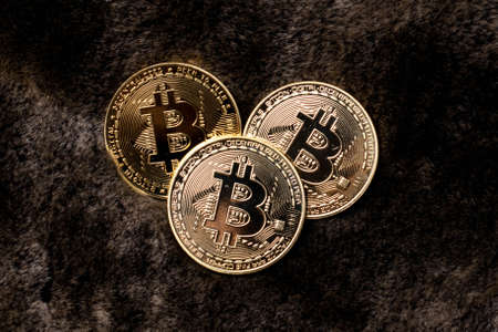 Three bitcoin coins of gold color on a background of dark furの写真素材