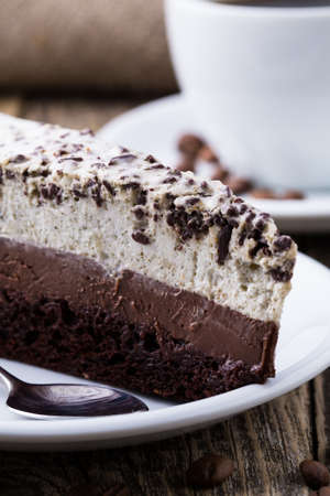 Slice of chocolate cake on the white plate with coffee beans on the wooden .