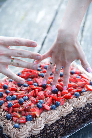 Couple hands with wedding rings and tasty wedding chocolate cake.
