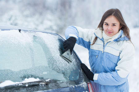 Woman remove snow from windshield with snow brush.