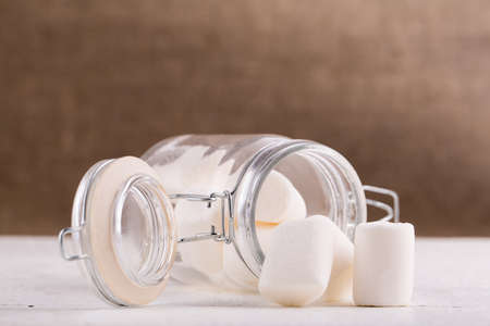 Marshmallows spilling from a storage jar, over wood background.