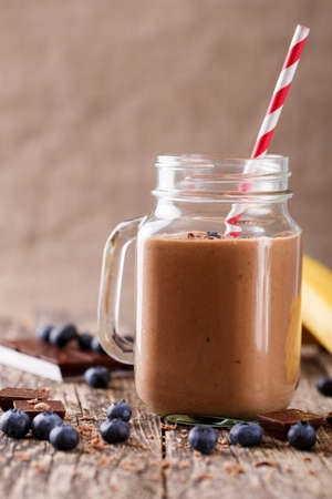 Tasty chocolate smoothie in glass jar with blueberries and chocolate pieces on table.の写真素材