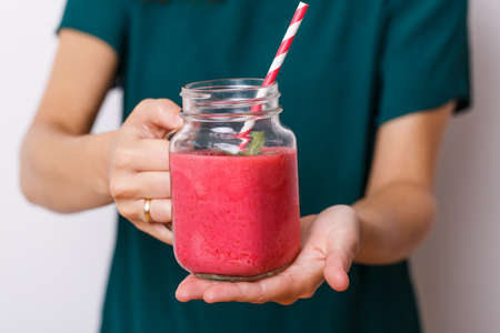 Young woman offer tasty smoothie in glass jar with drinking straw.の写真素材