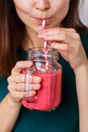 Young woman is drinking tasty smoothie in glass jar with drinking straw.の写真素材