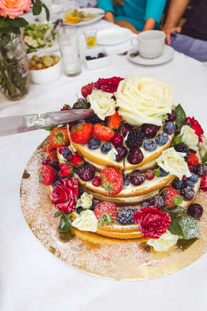 Tasty wedding cake with fruits and flowers on table.