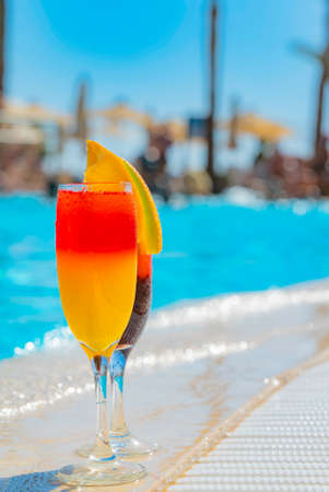 Two cocktails with natural juice and ice at the edge of the swimming pool. Orange cocktail with an...