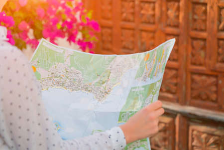 Girl holds a map in her hands, under the bush with flowers and in front of wooden door. Street of Garachico, Tenerife on a sunny day. Tourist woman study the map of locationの写真素材