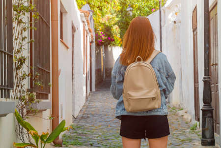 Girl with a backpack walk a narrow old street in a small town on Tenerife island. Redhead woman...