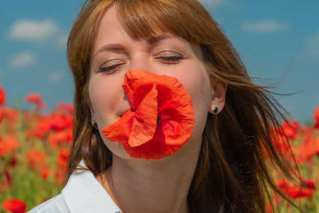 Young beautiful woman with a poppy flower in her mouth on a poppy field in summerの写真素材