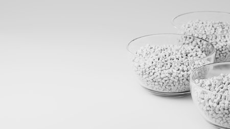 Glass cups with white plastic polypropylene granules, masterbatch polymer grain, on white backdrop....