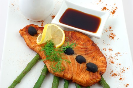 Salmon fried with spices with a lemon on a white plate with fennelの写真素材