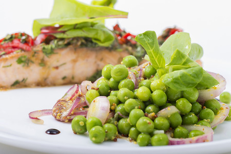 Peas and vegetables on a white dish red fish at small depth of sharpnessの写真素材