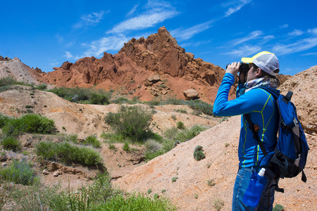 The traveller in jeans and a dark blue T-shirt observing of red rocks in the field-glass