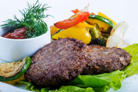 Fried meat with vegetables and sauce on a white dish close up.の写真素材