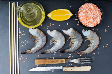 raw shrimp with knife and fork on a black stone background. view from aboveの写真素材