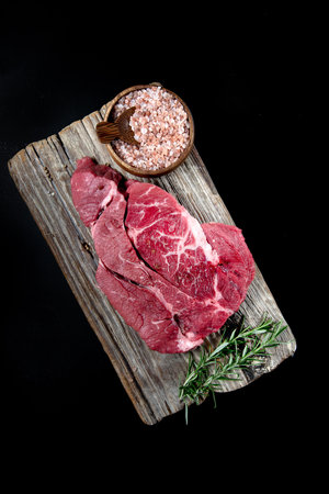 piece of fresh meat with salt on textured board on a black background from above