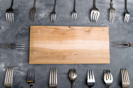 cutting board with space for an inscription as a background with forks on a gray backgroundの写真素材