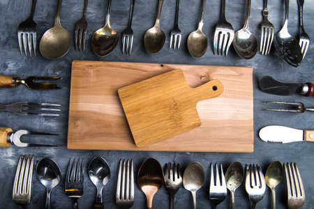 Frame made of steel cutlery on a gray background, top view. With cutting board and space for textの写真素材