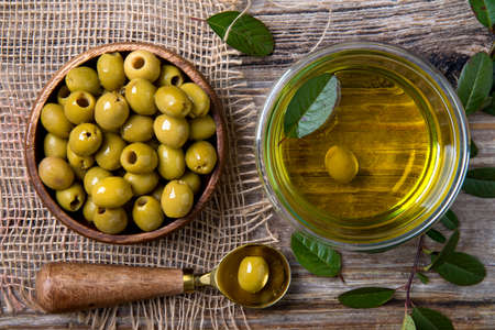 olive oil in a glass bowl. olives in a wooden cup on a burlap background. in a rustic style. view from aboveの写真素材