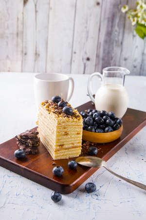slice of cake with blueberries and a carafe of milk on a white table