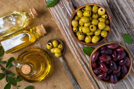 olive oil in bottles and olives in wooden bowls on a textured table top viewの写真素材