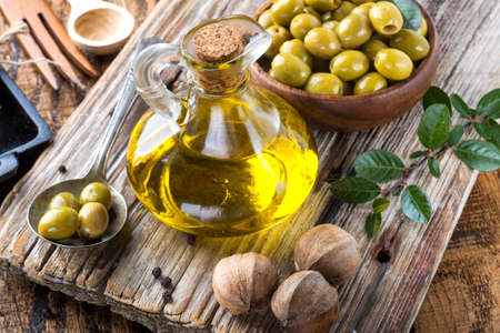 olive oil in a glass vessel and olives in a wooden bowl on a textured boardの写真素材