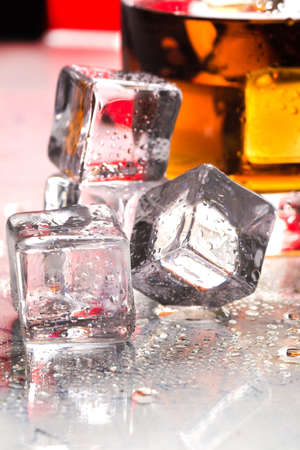 glass of whiskey on a glass table next to ice cubesの写真素材