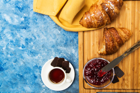 croissant with raspberry jam and coffee on a wooden stand on a blue table top viewの写真素材
