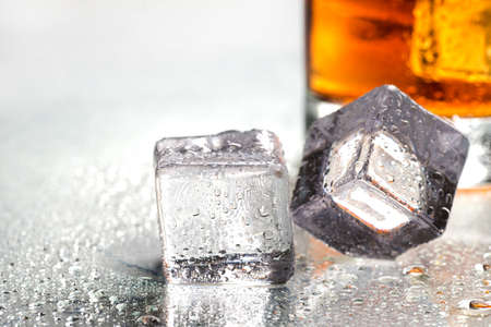 ice cubes on a glass table next to a glass of whiskey. close-up