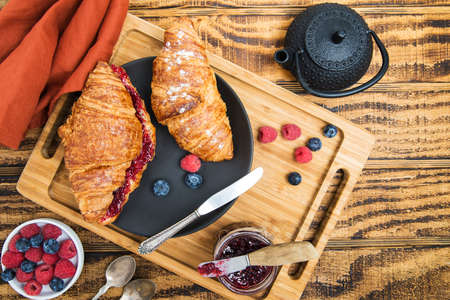 croissant with raspberry jam and tea on a wooden table. raspberries and blueberries. view from aboveの写真素材