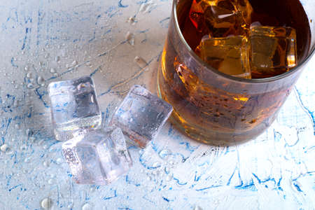 Golden whiskey in glass with ice cubes on table, top view. Space for text