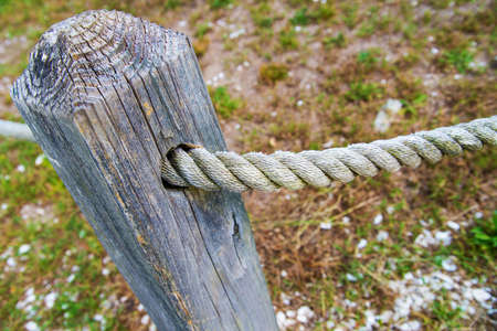 Rope fence fragment. An old gray rope going through a wooden post punished by the passage of time.