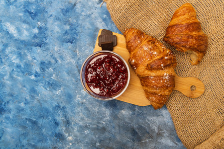 croissant with raspberry jam and chocolate on a wooden stand on a blue table top viewの写真素材