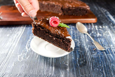 hand serves a piece of chocolate cake with raspberries on the cake spatula
