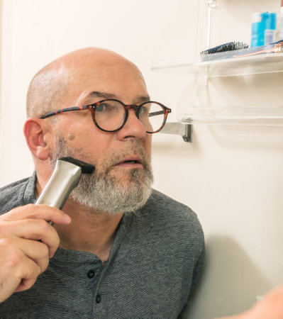 man shaves beard with trimmer or electric shaver at home. beauty, hygiene and shaving conceptの写真素材
