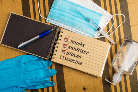 COVID-19. New rules of life. home exit plan concept. Notepad with medical mask, surgical gloves, syringe with vaccine and hand sanitizerの写真素材