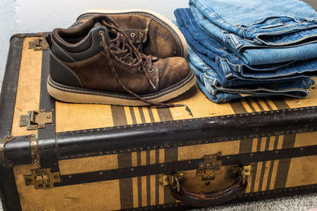 old shoes and stack of blue jeans lie on a vintage suitcase. The concept of travel and comfortable equipment.の写真素材