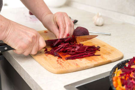 Closeup of hand with knife cutting fresh vegetable. chef cutting beet on a white cutting board closeup.の写真素材