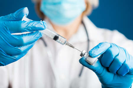 hands of a doctor in medical gloves draws a liquid vaccine against the corona virus covid 19 into a syringe from a vial preparing for injection. Influenza vaccination concept for coronavirus immunization.の写真素材