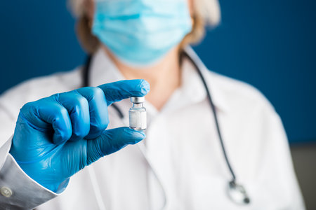 Doctor holding vial of vaccine - lab photo. Medical hands in blue gloves Making antiviral vaccine..の写真素材