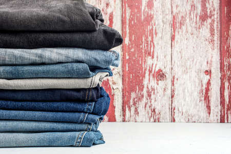 stack of different jeans on a white table against a wooden wall. Place for textの写真素材