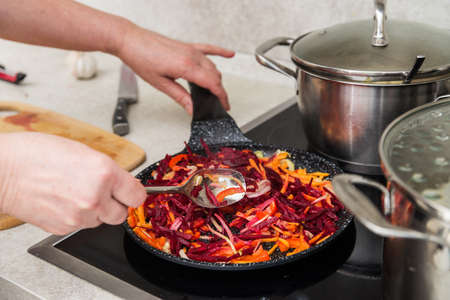 Close-up of a woman's hand mixing beets cut into cubes, carrots, garlic in a frying panの写真素材