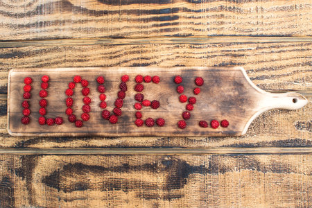 Bright letters of fresh raspberries, love you, on a cutting board
