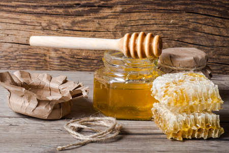 jar of honey with honeycomb and a dipper on wooden table.