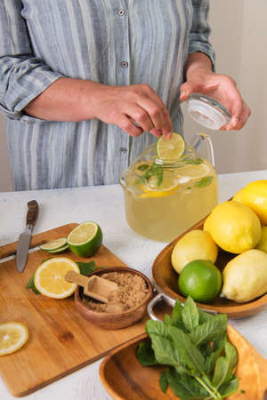 Woman's hands preparing homemade lemonade. Various ingredient, lime, lemon, mint on the kitchen table.の写真素材