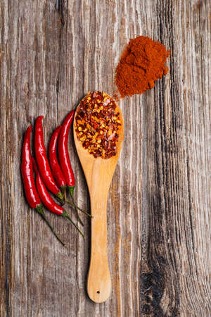 Ground red pepper in a wood spoon with fresh pepper pods on a textured wooden background. top view.