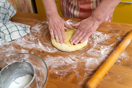 Women's hands are preparing dough for baking on the kitchen table in the home kitchen.