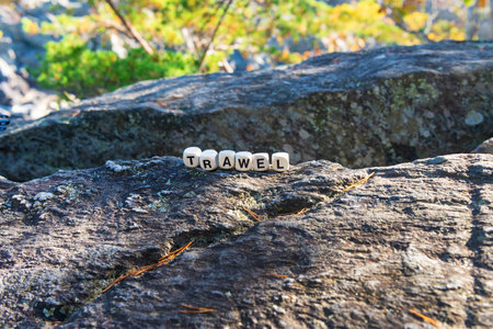 On a stone cliff in the mountains, the word travel is made up of wooden cubes.